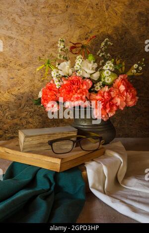 Stillleben mit einer Brille, die auf einem Buch ruht, und einer Blume in einer Vase. Stockfoto