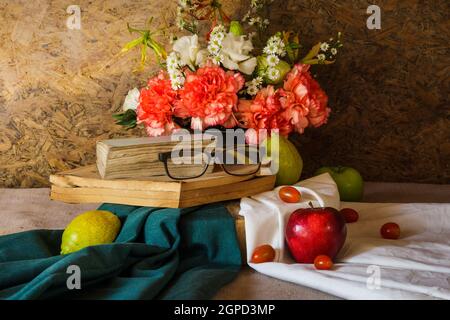 Stillleben mit Gläsern, die auf dem Buch ruhen, mit Früchten und Blumen in einer Vase. Stockfoto