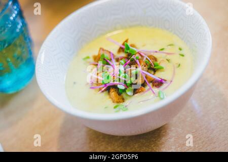 Nahaufnahme von frischer Brokkoli-Suppe mit knusprigen Croutons und Rettichsprossen in weißer Keramikschale Stockfoto