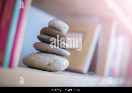 Feng Shui: Steinkairn zu Hause in einem Bücherregal, verschwommene Bücher im Vorder- und Hintergrund. Balance und Entspannung. Sonnenlicht. Stockfoto