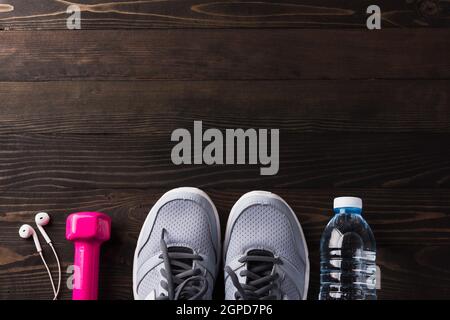 Paar Sportschuhe, Kopfhörer, Hantel und Wasserflasche auf schwarzem Holztisch Hintergrund, Grau Sneaker und Zubehör-Geräte in Fitness-STUDIO, Healt Stockfoto