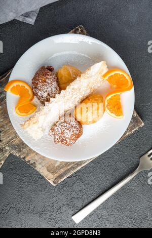 Karnevalsbonbons auf einem weißen Teller auf schwarzem Hintergrund serviert. Sfrappole oder chiacchiere oder Engelsflügel. Castagnole, ein Teig gebraten und bedeckt wi Stockfoto