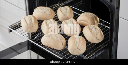 Metallregal auf Geländern mit aufgestellten rohen Brotbrötchen Vor dem Backen in der Küche Stockfoto