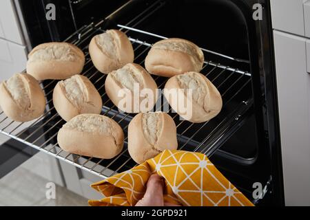 Von oben gesichtslose Person mit Handtuch entfernen heißen Glide Rack Mit frischen Brötchen aus dem Ofen Stockfoto