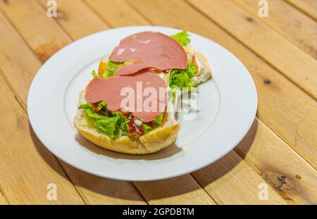 Bologna-Sandwich mit Salat, Brot, Mayonnaise und Ketchup. Natürliche und alternative Lebensmittel. Das Sandwich ist einer der bekanntesten und vielseitigsten Snacks Stockfoto