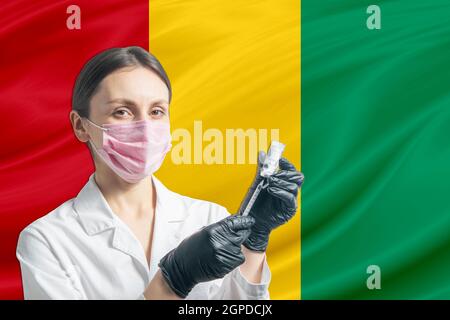 Ärztin bereitet die Impfung vor dem Hintergrund der Guinea-Flagge vor. Impfkonzept Guinea. Stockfoto