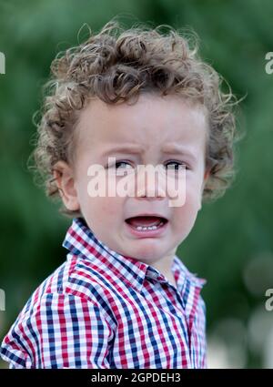 Traurig Baby mit lockigem Haar weinend im Garten Stockfoto