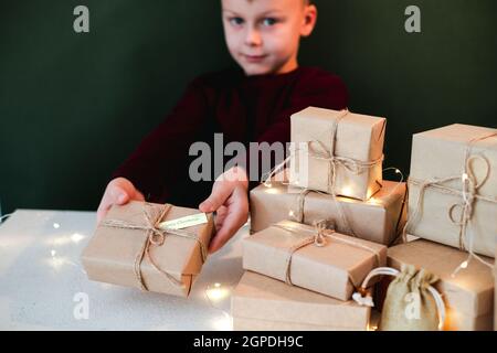 Kind hält ein handgemachtes Weihnachtsgeschenk in Kraftpapier verpackt. Neujahrs- und Weihnachtskonzept ohne Verschwendung. Hochwertige Fotos Stockfoto