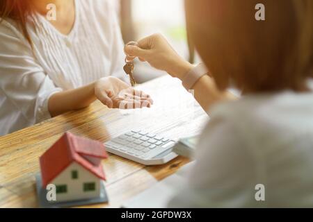 Ein neuer Vermieter erhält eine Schlüsselkette von einem Immobilienmakler, nachdem er eine Hauskaution bezahlt hat. Immobilienmakler und Kunde, Immobilieninvestition. Stockfoto