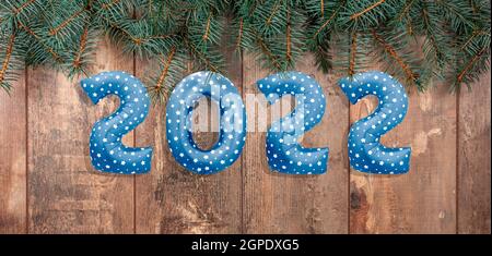 2022 Ballontext auf rustikalem Holztisch mit Zweigen von Weihnachtsbäumen. Happy New Year Eve Einladung mit Weihnachten blauen Folienballons 2022. Flach Stockfoto