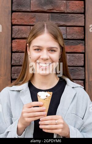 Happy blonde Mädchen mit Eiscreme stehen an einer Ziegelwand und schaut dich an Stockfoto