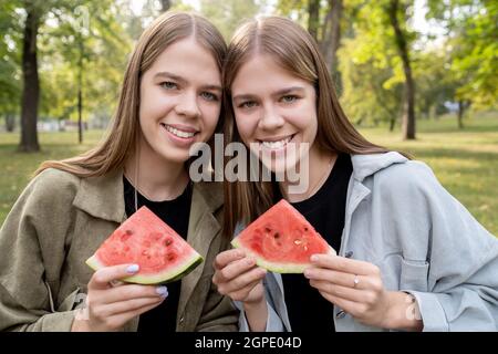 Zwei niedliche Mädchen mit Wassermelonenscheiben, die am Sommertag im Park ruhen Stockfoto