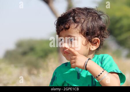 Nahaufnahme eines jungen Kindes aus einer indischen Bauernfamilie, die auf dem Feld steht und mit Fingergesten ein entferntes Objekt anschaut Stockfoto