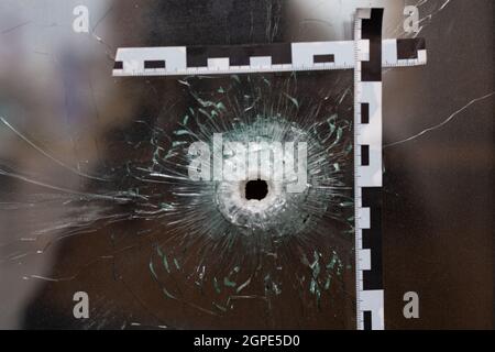 Einschusslöcher in einem Glasfenster, das mit einem Polizeiband markiert ist. Stockfoto