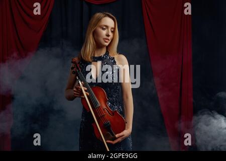 Die Geigerin hält Bogen und Violine im Retro-Stil. Frau mit Streichmusikinstrument, Musikkunst, Musikerspiel auf Viola, dunkler Hintergrund Stockfoto