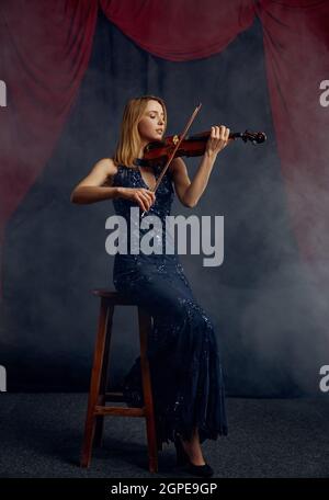 Violinistin mit Bogen und Violine, Solokonzert auf der Bühne. Frau mit Streichinstrument, Musiker spielen auf Viola, dunkler Hintergrund Stockfoto