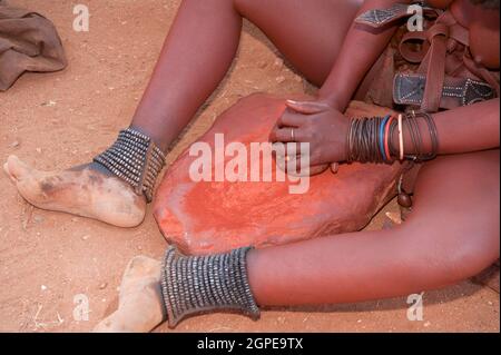 Frau Himba zerquetscht roter Tonerde, dieser wird dann verwendet, um Ihr Haar auftragen. In einem Himba Dorf fotografiert, Epupa Wasserfälle, Kaokoveld, Namibia, Afrika Stockfoto