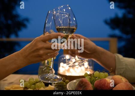 Junger Mann und Frau toasten über servierten Tisch während des romantischen Abendessens im Freien Stockfoto