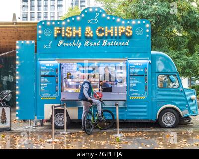 Ein Mann auf einem Fahrrad, der im Herbstregen darauf wartet, dass eine Dame in einem umgebauten Fish & Chips-Van, der in South Bank, London, England, geparkt ist, Essen serviert. Stockfoto