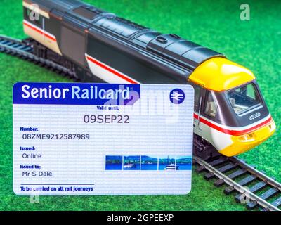 Nahaufnahme einer Senior Railcard (gültig in Großbritannien für ermäßigte Bahnpreise für Personen ab 60 Jahren), die sich auf einer Strecke gegen einen Modell-/Spielzeugzug lehnt. Stockfoto