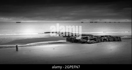 Schwarz-weißes Bild von einer Einzelperson, die an den 6. Juni 1944 erinnert. Mit Maulbeerhafen bleibt am Strand. Stockfoto