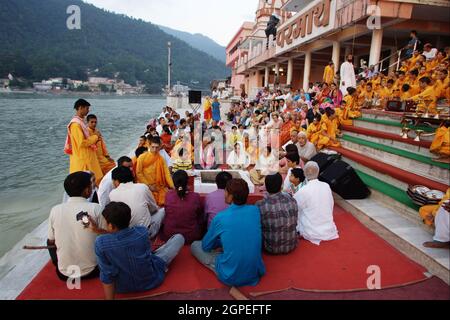 Zuschauer, Gläubige, Anhänger und Priester in orangefarbenen Gewändern in der heiligen Stadt Rishikesh in Uttarakhand, Indien während der abendlichen Lichtzeremonie cal Stockfoto