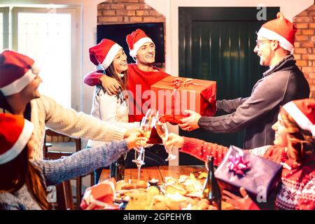 Freunde mit weihnachtshut geben einander Weihnachtsgeschenk - Champagner Wein Toast auf Haus Weihnachten Dinner Party - Feiertagskonzept mit Menschen Spaß haben Stockfoto