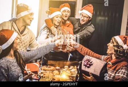 Freunde Gruppe mit santa Hüte Austausch Weihnachtsgeschenke mit Champagner Wein Toast zu Hause Abendessen - Winterurlaub Konzept mit jungen Menschen Stockfoto