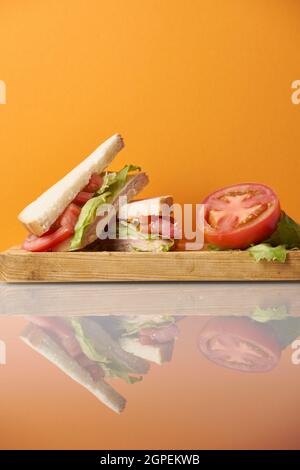 Gesundes Schinken-Käse-Sandwich mit Tomaten und Salat auf orangefarbenem Hintergrund Stockfoto