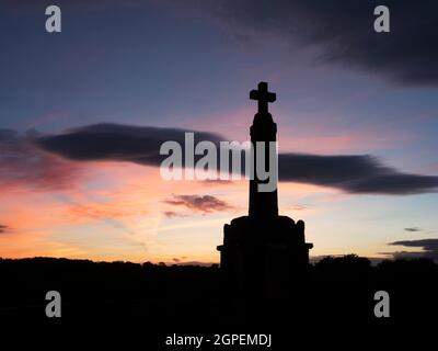 Kreuzartige Kriegsdenkmal, das vor einem Sonnenuntergangshimmel auf der Herbst-Tagundnachtgleiche Knaresborough North Yorkshire England geschildert wurde Stockfoto