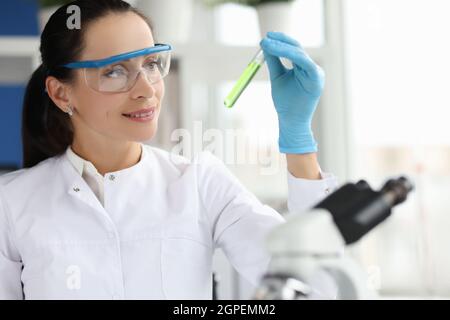 Porträt einer lächelnden Wissenschaftlerin mit einer Brille, die im Labor ein chemisches Reagenzglas hält Stockfoto