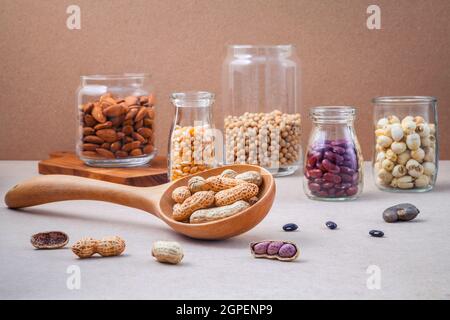 Verschiedene Bohnen und Nüsse in das Glas auf braunen Hintergrund. mung Bean, Erdnuß, rote Kidney-bohnen, Lotus Samen, Mandel, Hirse und Braun pinto Bohnen. Stockfoto