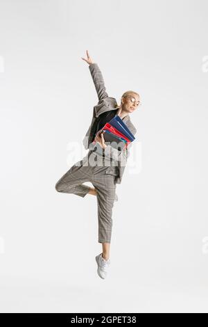 Porträt einer Mitarbeiterin in voller Länge in klassischem Anzug mit einem Ordner, der wie eine Ballerina auf weißem Hintergrund springt Stockfoto