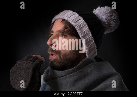 Mann aus dem mittleren Alter mit fingerlosen Handschuhen und Strickmütze auf schwarzem Hintergrund Stockfoto