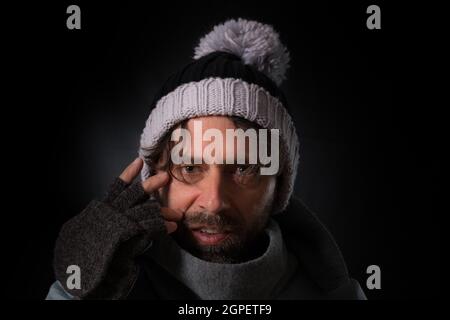 Mann aus dem mittleren Alter mit fingerlosen Handschuhen und Strickmütze auf schwarzem Hintergrund Stockfoto