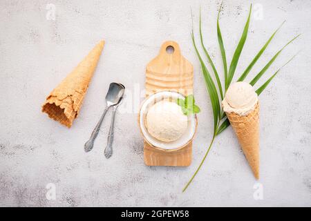 Kokoseis Aromen in der Hälfte der Kokosnuss Setup auf weißem Stein Hintergrund. Sommer und Süße Menükonzept. Stockfoto