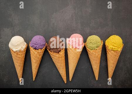 Verschiedene Eis Geschmack in Zapfen Heidelbeere, Pistazie, Mandel, Orange und Schokolade Setup auf dunklen Stein Hintergrund. Sommer und Süße Menükonzept Stockfoto