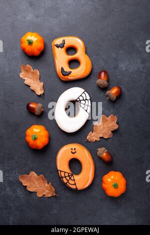 Text BOO aus Lebkuchengebäck mit dekorativen Kürbissen und trockenen Eichenblättern auf dunklem Steingrund. Halloween-Konzept - Bild Stockfoto