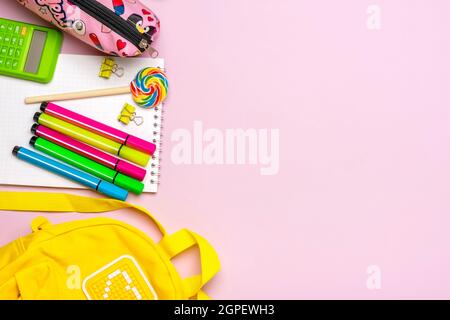 Zurück zur Schule, Bildungskonzept. Gelber Rucksack mit Schulbedarf - Notizbuch, Stifte, Clips, Schere isoliert auf rosa Hintergrund Draufsicht Copy Stockfoto