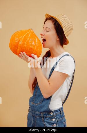 Die Bäuerin beißt einen reifen, süßen Kürbis auf beigefarbenem Hintergrund. Stockfoto