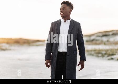 Schöner, stilvoller schwarzer Mann in klassischem weißen Hemd, Hose und Mantel, posiert im Freien bei Sonnenuntergang, erfolgreicher Mann, Modekonzept, Herrenmode, Klasse Stockfoto