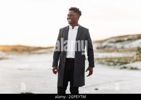 Schöner, stilvoller schwarzer Mann in klassischem weißen Hemd, Hose und Mantel, posiert im Freien bei Sonnenuntergang, erfolgreicher Mann, Modekonzept, Herrenmode, Klasse Stockfoto