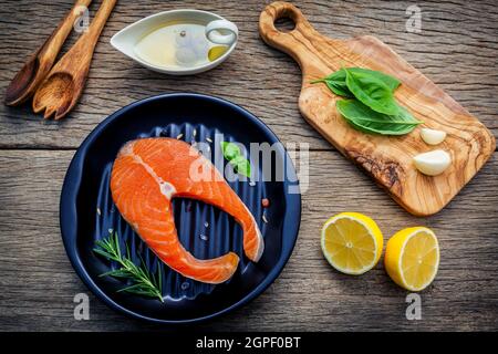 Rohes Lachsfilet in die schwarze Platte mit Zutaten Olivenöl, Himalaya Salz und Kräuter Basilikum, Fenchelsamen, Rosmarin, Knoblauch, schwarzer Pfeffer ein Stockfoto