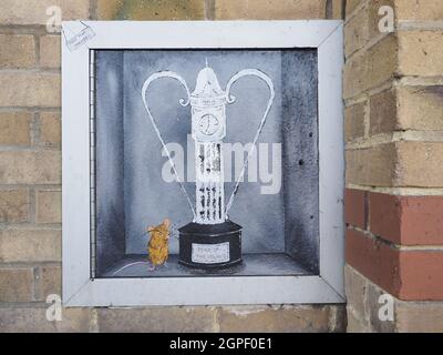 Sheerness, Kent, Großbritannien. September 2021. Ein weiteres neues Kunstwerk ist aus Sheppeys 'Banksy' erschienen. Ein Mystery-Künstler hat ein weiteres ihrer Gemälde mit ihrer Unterschrift "Moo Mop" Maus Charakter geschaffen. Die neueste zeigt die Maus mit einer Trophäe, die wie die Stadtuhr gestaltet ist, an einer Wand nahe dem Eingang zu Tesco. Kredit: James Bell/Alamy Live Nachrichten Stockfoto