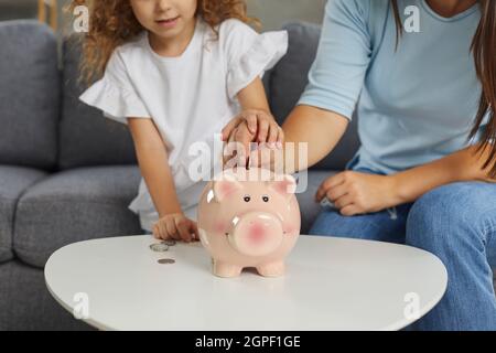 Mutter und Tochter, die planen, etwas Geld zu sparen, indem sie Münzen in Sparschwein stecken Stockfoto