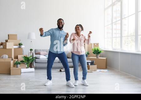 Zufriedenes junges afroamerikanisches Paar, das in der Wohnung mit Pappkartons im häuslichen Interieur tanzt, freier Raum Stockfoto