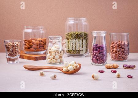 Verschiedene Bohnen und Nüsse in das Glas auf braunen Hintergrund. mung Bean, Erdnuß, rote Kidney-bohnen, Lotus Samen, Mandel, Hirse und Braun pinto Bohnen. Stockfoto