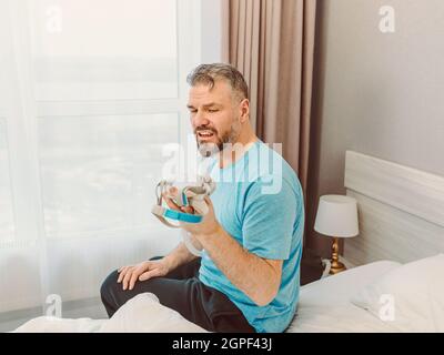 Reifer glücklicher Mann mit chronischen Atemproblemen erwägt die Verwendung CPAP-Maschine auf dem Bett im Schlafzimmer sitzen. Gesundheitswesen, CPAP, Schnarchen Konzept Stockfoto
