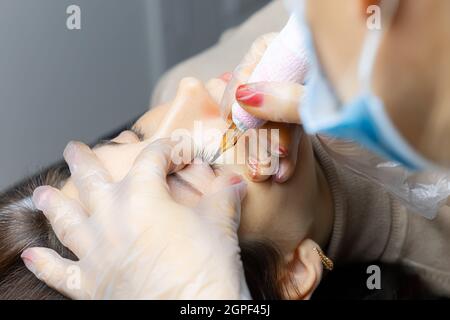 Der Meister der permanenten Make-up sitzt am Kopf des Bettes und führt das Verfahren der Augenlid Tätowierung Stockfoto