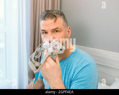 Reifer glücklicher Mann mit chronischen Atemproblemen erwägt die Verwendung CPAP-Maschine auf dem Bett im Schlafzimmer sitzen. Gesundheitswesen, CPAP, Schnarchen Konzept Stockfoto